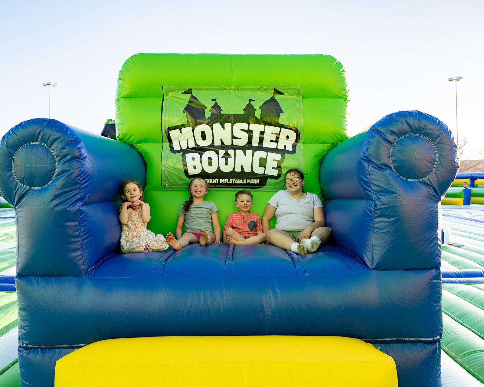 Little kids smiling and sitting on a giant inflatable chair on one of the world's largest bounce houses