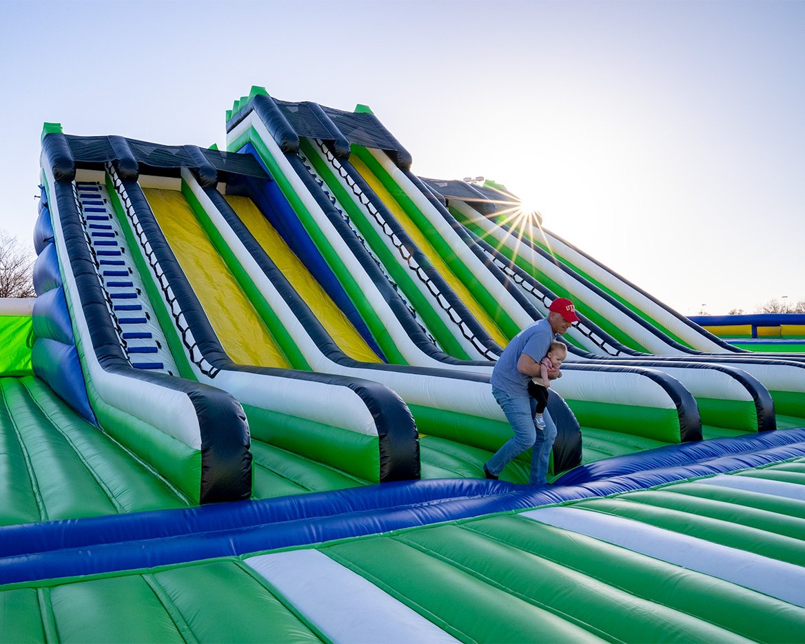 Man carrying a baby next to a set of giant inflatable slides at one of the world's largest bounce houses